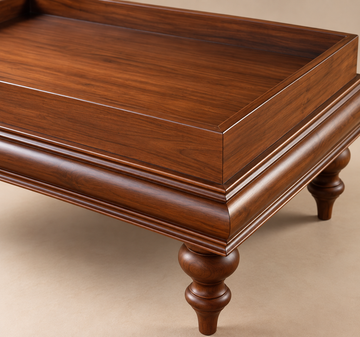 A close-up of a polished dark brown wooden table with a rectangular tray top, decorative molding, and turned legs on a neutral beige background.